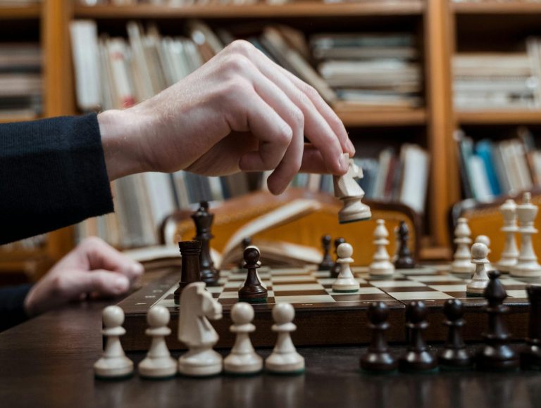 Close-up of a hand making a chess move in a library, focusing on strategy.