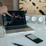 A businessman points to a stock chart on a laptop screen, indicating market analysis insights.